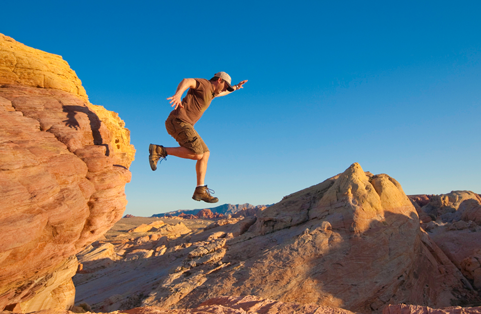 A man leaps down from a mountain.